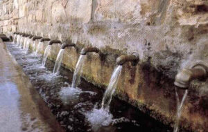 Filas de caños de piedra que vierten agua clara en un canal mostrando posibilidades de reutilizacion de agua.