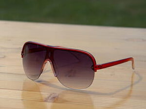 Gafas de sol aviador con montura roja y lentes degradadas sobre una mesa de madera, sonometro