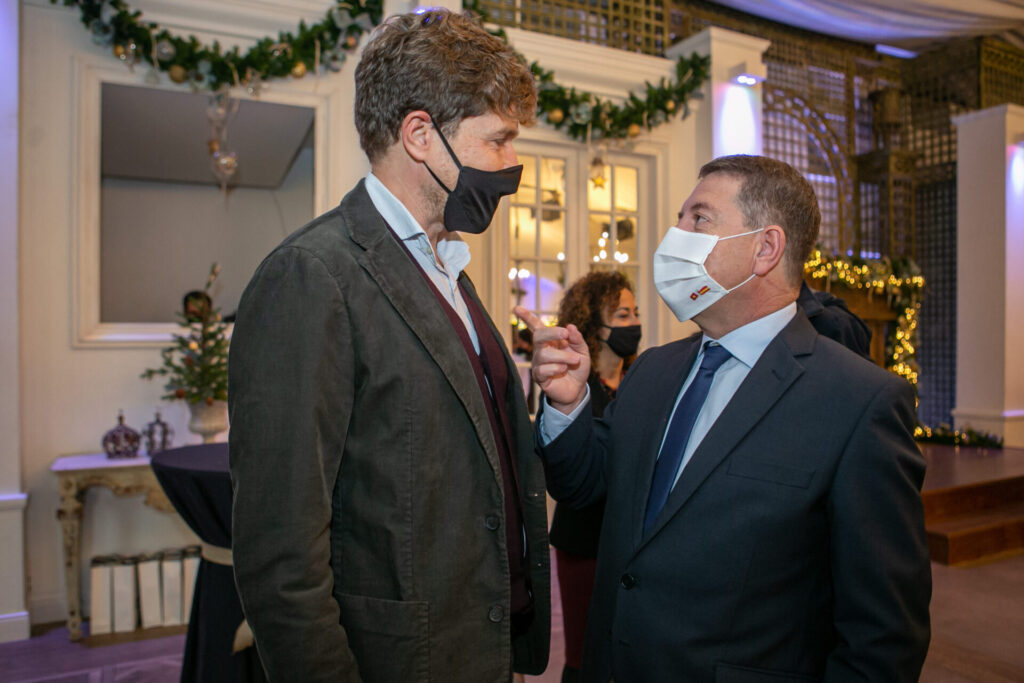 Dos personas con mascarillas hablan en un evento interior decorado, evocando sostenibilidad y responsabilidad ambiental