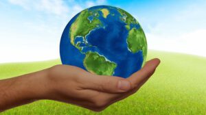 Mano sosteniendo un globo terráqueo sobre un campo verde que simboliza sostenibilidad 7