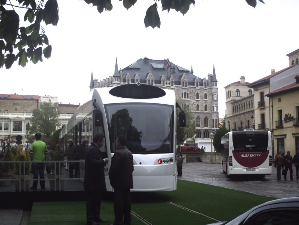 Tranvía moderno estacionado en una plaza junto a autobuses y edificios históricos, demostrando sostenibilidad urbana
