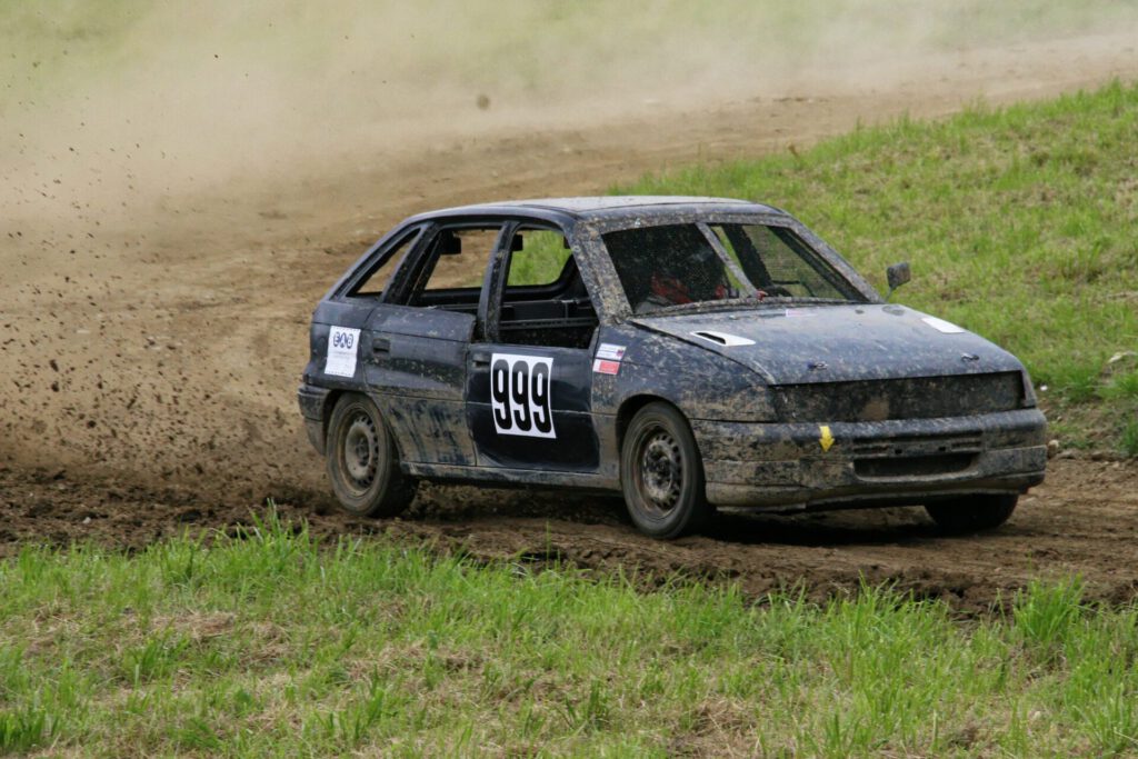 Coche de rally cruzando una curva sobre suelo compactado con salpicaduras de barro