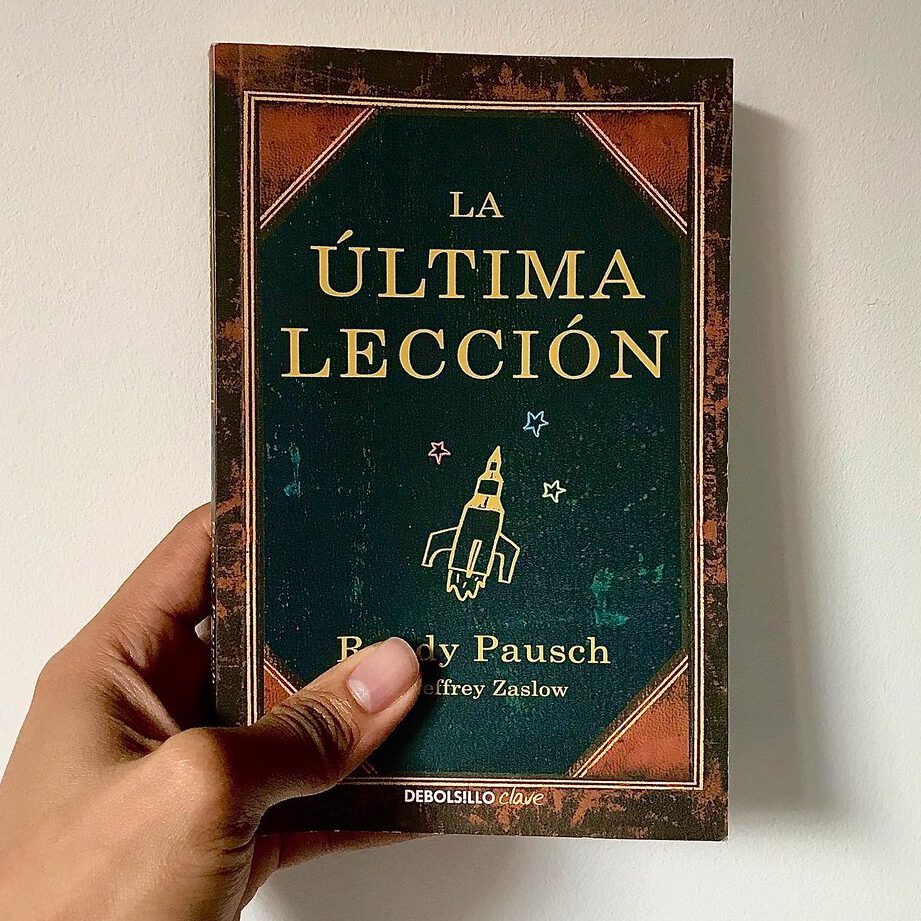 Mano sosteniendo un libro de portada verde con ilustración de cohete que evoca el paso del tiempo.