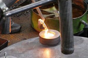 Vertido de vidrio fundido en un molde circular con cucharón metálico sobre una mesa de taller
